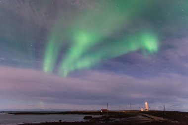 Yeşil Aurora Borealis okyanus ile İzlanda'daki Grotta deniz feneri ve bir siyah kum plaj ön planda