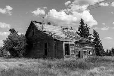 Saskatchewan, Kanada siyah ve beyaz ağaçlar, uzun ot ve gökyüzü ile çevrili eski terk edilmiş çayır çiftlik evi