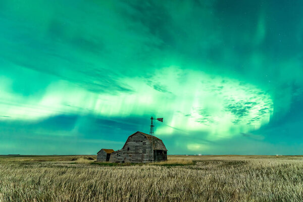 Swirl of bright Northern Lights over vintage barn, bins, windmill and stubble in Saskatchewan, Canada