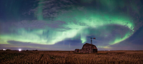 Swirl of bright Northern Lights over vintage barn, bins, windmill and stubble in Saskatchewan, Canada