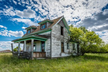 Saskatchewan, Kanada 'da ağaçlar, çimenler ve mavi gökyüzü olan terk edilmiş eski çayır çiftlik evi.