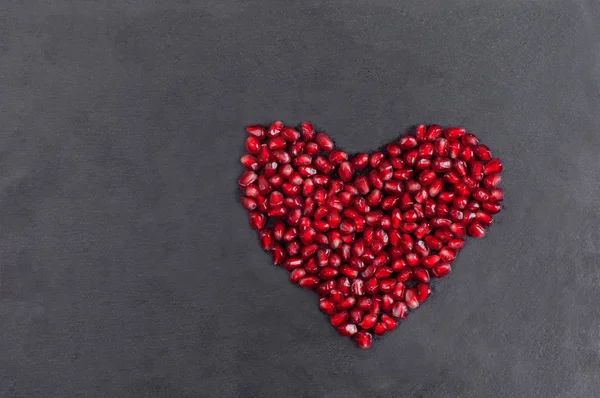 big Heart of fresh pomegranate on a background of dark stone Closeup. Romantic Valentines day concept.