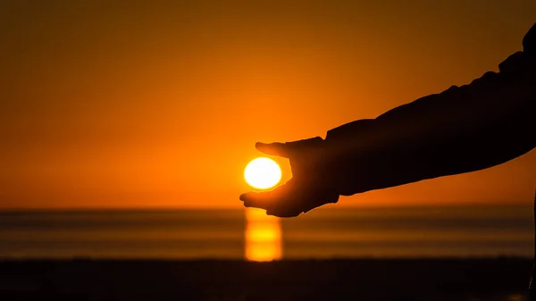 Hand catching the sun during the sunset, detail of the hand and the sun in the coast of the Pacific Ocean