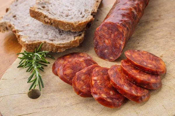 Chouriço ibérico, chouriço espanhol ou linguiça espanhola cortada em fatias em uma tábua de madeira com pão rústico — Fotografia de Stock