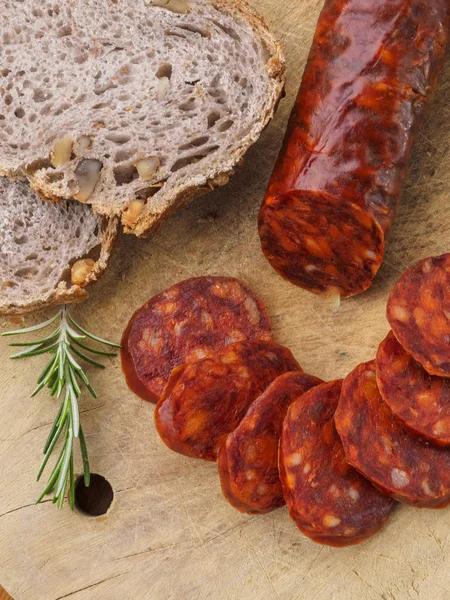 Chouriço ibérico, chouriço espanhol ou linguiça espanhola cortada em fatias em uma tábua de madeira com pão rústico — Fotografia de Stock