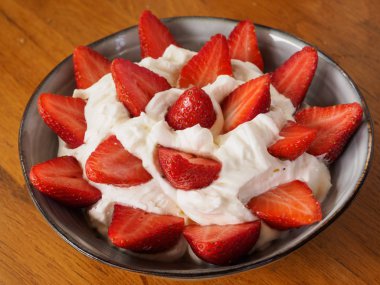 Ahşap arka plan ile seramik bir kapta krem ile çilek