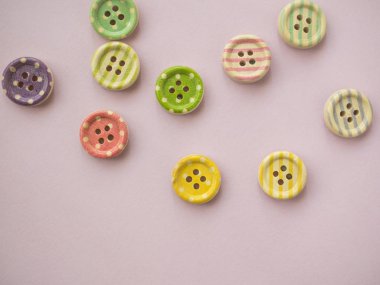 Renkli çizgili ahşap düğmeler ve pastel pembe arka planda renkli noktalar.