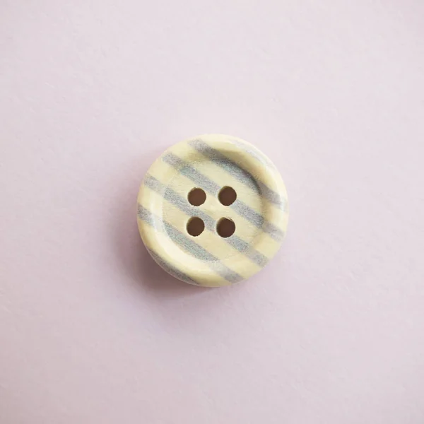 Isolated wooden button with colored colorful stripes on a light pink background