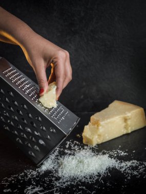 Siyah bir arka plan üzerinde parmesan peyniri rendeleyen bir kadının eli. Koyu gıda