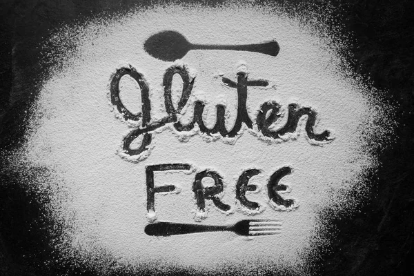 Gluten free flour with text gluten free in English language with spoon and fork silhouette made with flour on dark texture background