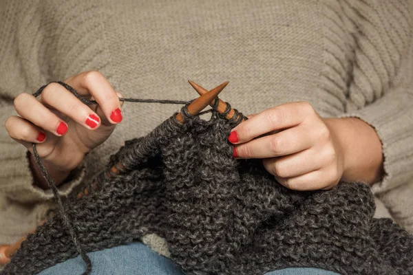 Girl with red nails knitting dark gray wool with wooden needles