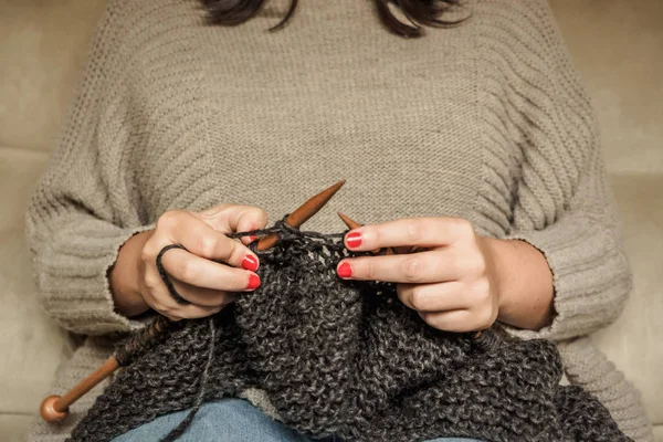 Girl with red nails knitting dark gray wool with wooden needles
