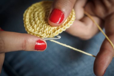 Sarı iplik ve çivi kırmızı boyalı tığ işi yapan kız