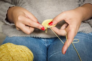 Sarı iplik ve çivi kırmızı boyalı tığ işi yapan kız