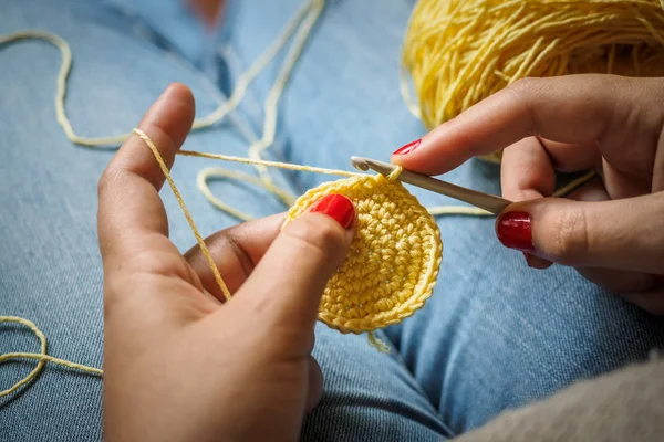 Girl doing crochet with yellow yarn and nails painted red