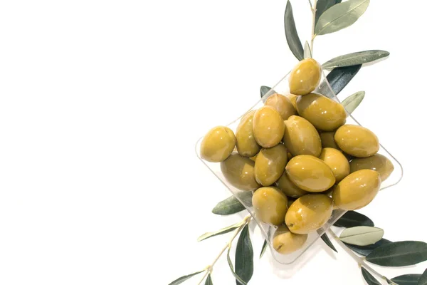 Группа зеленых блестящих оливок в квадратной пластиковой пластине и три бранча оливкового дерева — стоковое фото