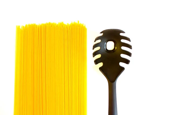 Длинные сырые желтые спагетти и черная ложка с изолированной на белом дырой — стоковое фото