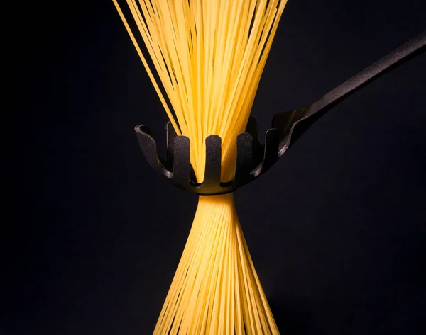 Сырые длинные желтые спагетти в черной ложке изолированы на черном — стоковое фото