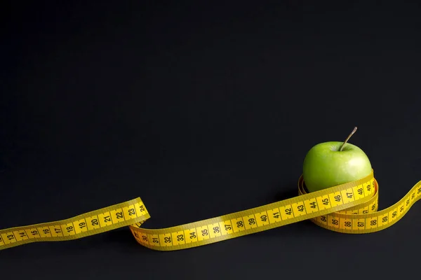 Grüner Apfel und Maßband mit Zentimetern und Zoll isoliert auf schwarzem Hintergrund — Stockfoto