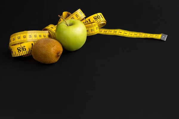 Manzana verde, kiwi y cinta métrica con centímetros y pulgadas aislados sobre fondo negro — Foto de Stock