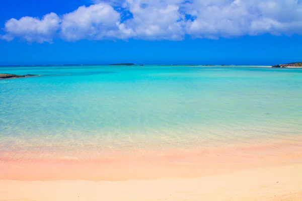 Plage avec sable rose et eau turquoise et nuages dans le ciel bleu. Photo De Stock
