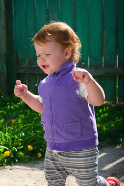 Küçük kızıl saçlı kız, bir yaşında, yaşını çalışır yard bir sıcak yaz gününde birçok dandelions ve yeşil çim onun etrafında büyümek.