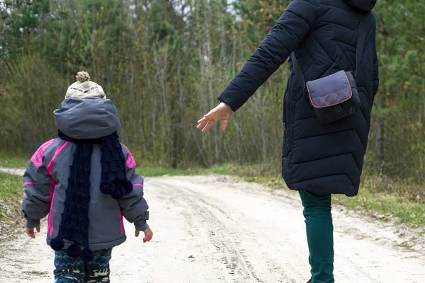 Mãe e filha estão andando na floresta de primavera. bebê e mãe caminham ao longo da estrada da floresta pela mão — Fotografia de Stock