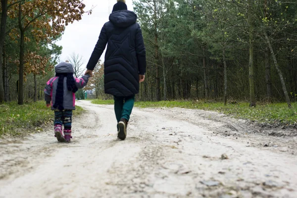 Mãe e filha estão andando na floresta de primavera. bebê e mãe caminham ao longo da estrada da floresta pela mão — Fotografia de Stock
