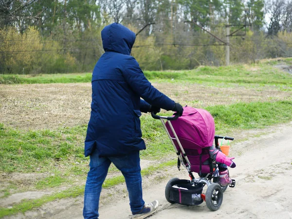 O pai caminha com a filha num carrinho de bebé. O pai com uma menina para passear. bebê em uma bicicleta pequena — Fotografia de Stock