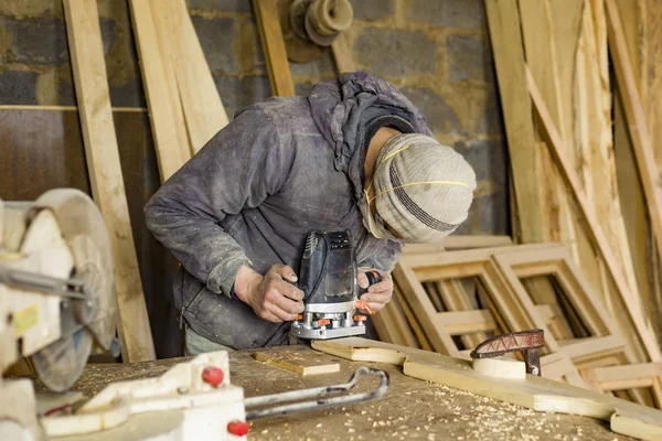 Un uomo fabbrica legno in un laboratorio di lavorazione del legno, un falegname in un respiratore con una fresatrice — Foto Stock