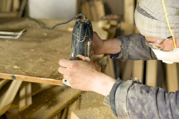 Un uomo fabbrica legno in un laboratorio di lavorazione del legno, un falegname in un respiratore con una fresatrice — Foto Stock