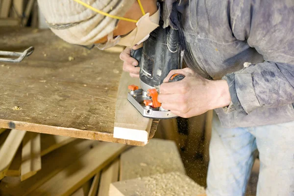 Un uomo fabbrica legno in un laboratorio di lavorazione del legno, un falegname in un respiratore con una fresatrice — Foto Stock