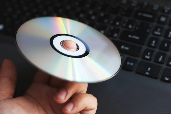 O disco compacto driver CD está girando no dedo indicador contra o fundo de um computador — Fotografia de Stock