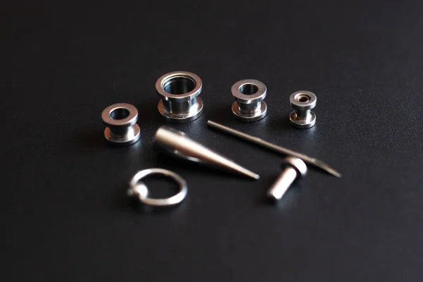 Conjunto de acessórios para piercing em um fundo escuro — Fotografia de Stock