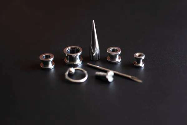 Acessórios piercing em um fundo preto jóias de metal inoxidável para os amantes de perfuração — Fotografia de Stock