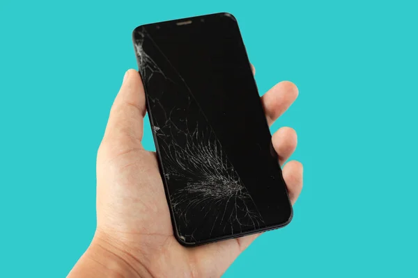 black broken phone in hand on aquamarine  background cracked touchscreen screen