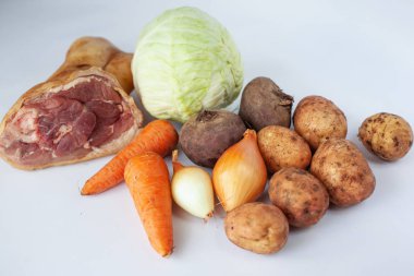 Borscht için taze malzemeler: patates, lahana, pancar, havuç, domuz bacağı ve beyaz arka plan soğan