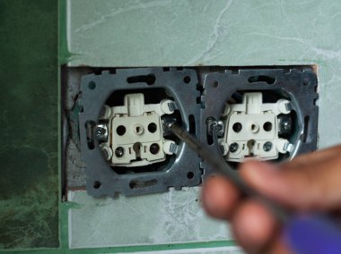 taç tarafından oyulmuş nişlerde soketlerin montajı, elektrikçi bir tornavida ile banyoda duvar prizleri giderir