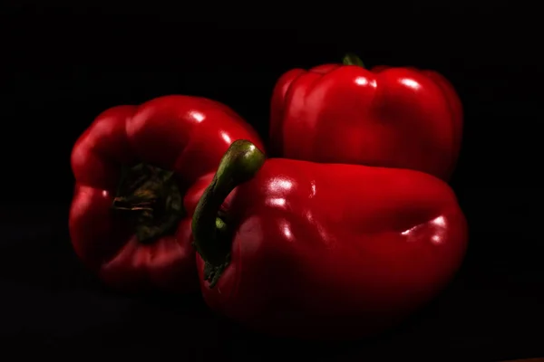 Três pimentas vermelhas doces (páprica) em fundo preto com pouca luz — Fotografia de Stock