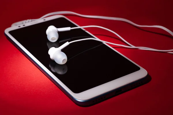 Concept: listen to music from the phone.smartphone with white headphones on a red background — Stock Photo, Image