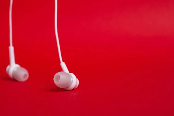Concept: white headphones (earphones) on a red background with copy space close up
