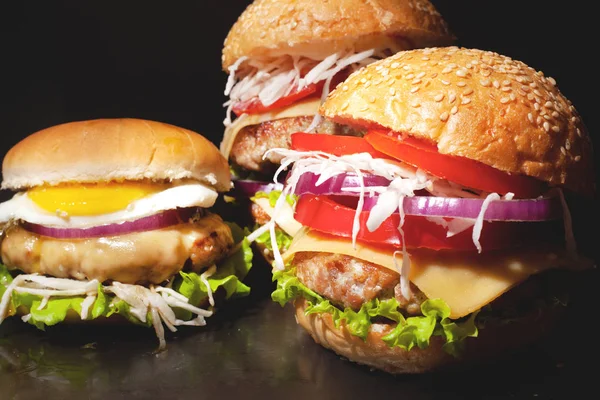 Концепция: фаст-фуд большие гамбургеры на черном столе. Большой двойной чизбургер с котлетами из говядины и свежими овощами, состав: перец, лук, помидоры, яйцо, салат, сыр на тёмном фоне . — стоковое фото