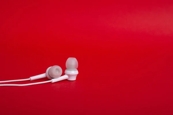 Conceito: fones de ouvido brancos (fones de ouvido) em um fundo vermelho com copyspace — Fotografia de Stock