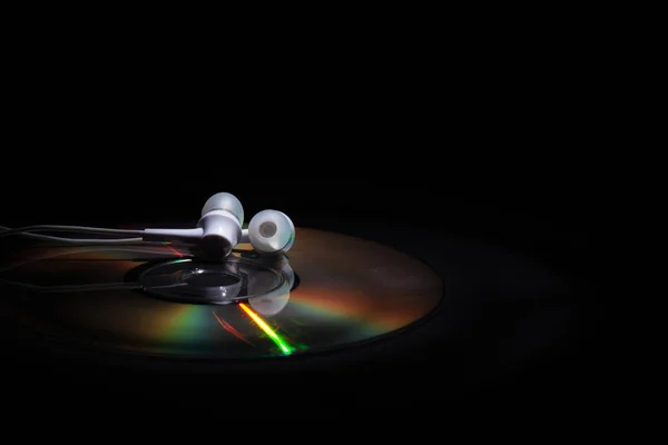 CD compact disk e cuffie bianche su sfondo scuro. concetto: ascoltare musica — Foto Stock