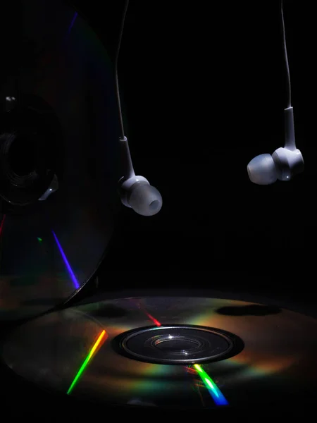 Disco compacto e fones de ouvido brancos em um fundo escuro. ouvir música no disco de CD — Fotografia de Stock