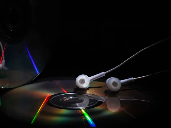 CD compact disk e cuffie bianche su sfondo scuro. concetto: ascoltare musica — Foto Stock