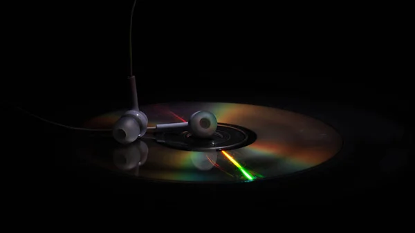 Компакт-диск і білі навушники на темному фоні — стокове фото