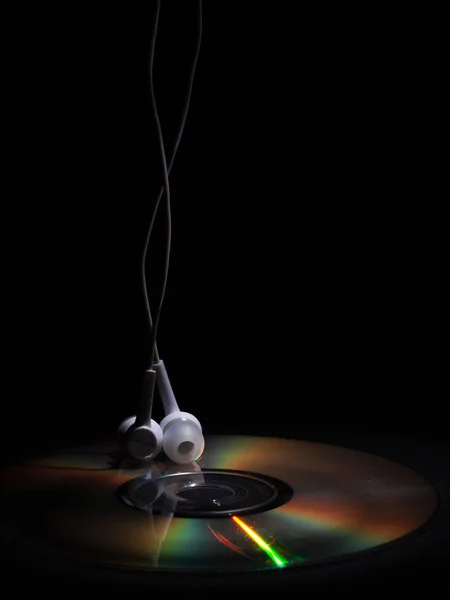 CD compact disk e cuffie bianche su sfondo scuro. concetto: ascoltare musica — Foto Stock
