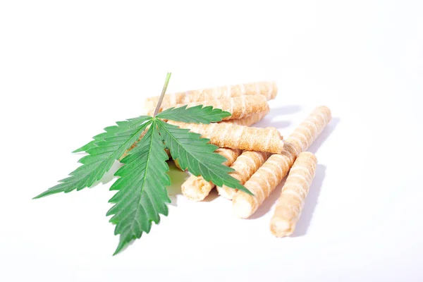 Galletas dulces en forma de tubos y una hoja de marihuana sobre un fondo blanco, confitería de cannabis —  Fotos de Stock