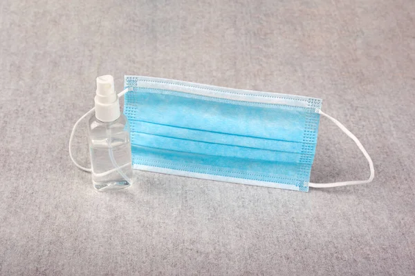 Orvosi kék maszk és kézfertőtlenítő palack fehér háttéren közelkép. egészség, higiénia, kovid-19 elleni védelem — Stock Fotó